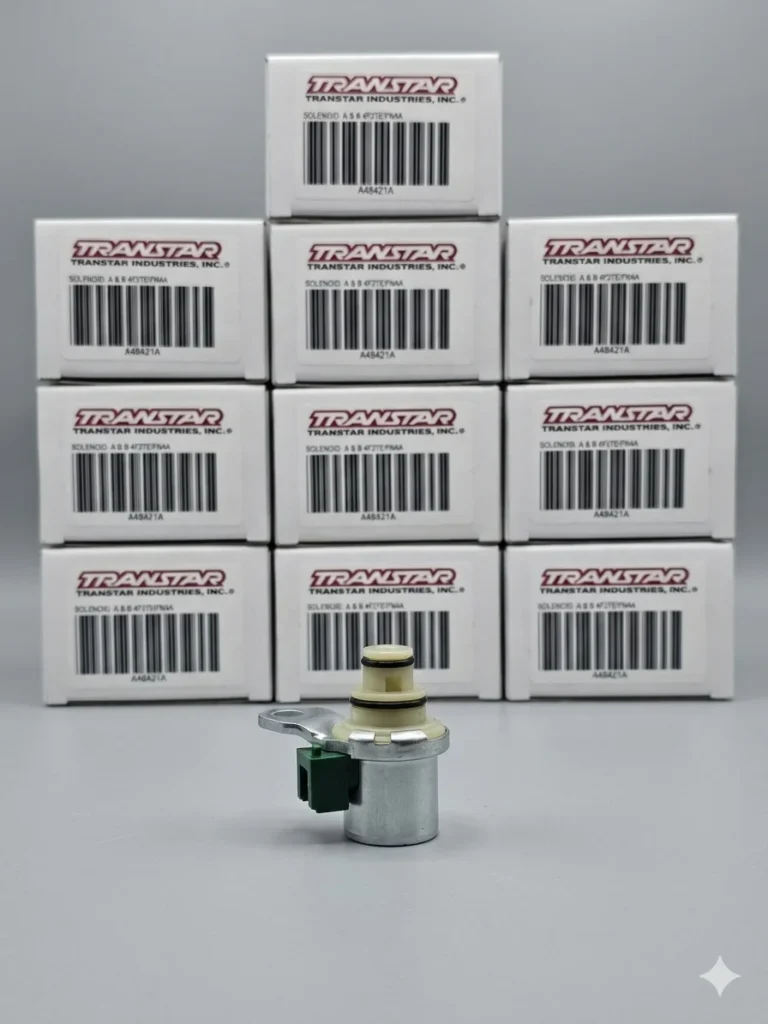 Electroválvula de transmisión Mazda con conector verde en primer plano. Al fondo, 10 cajas blancas de la marca Transtar apiladas con códigos de barras visibles.